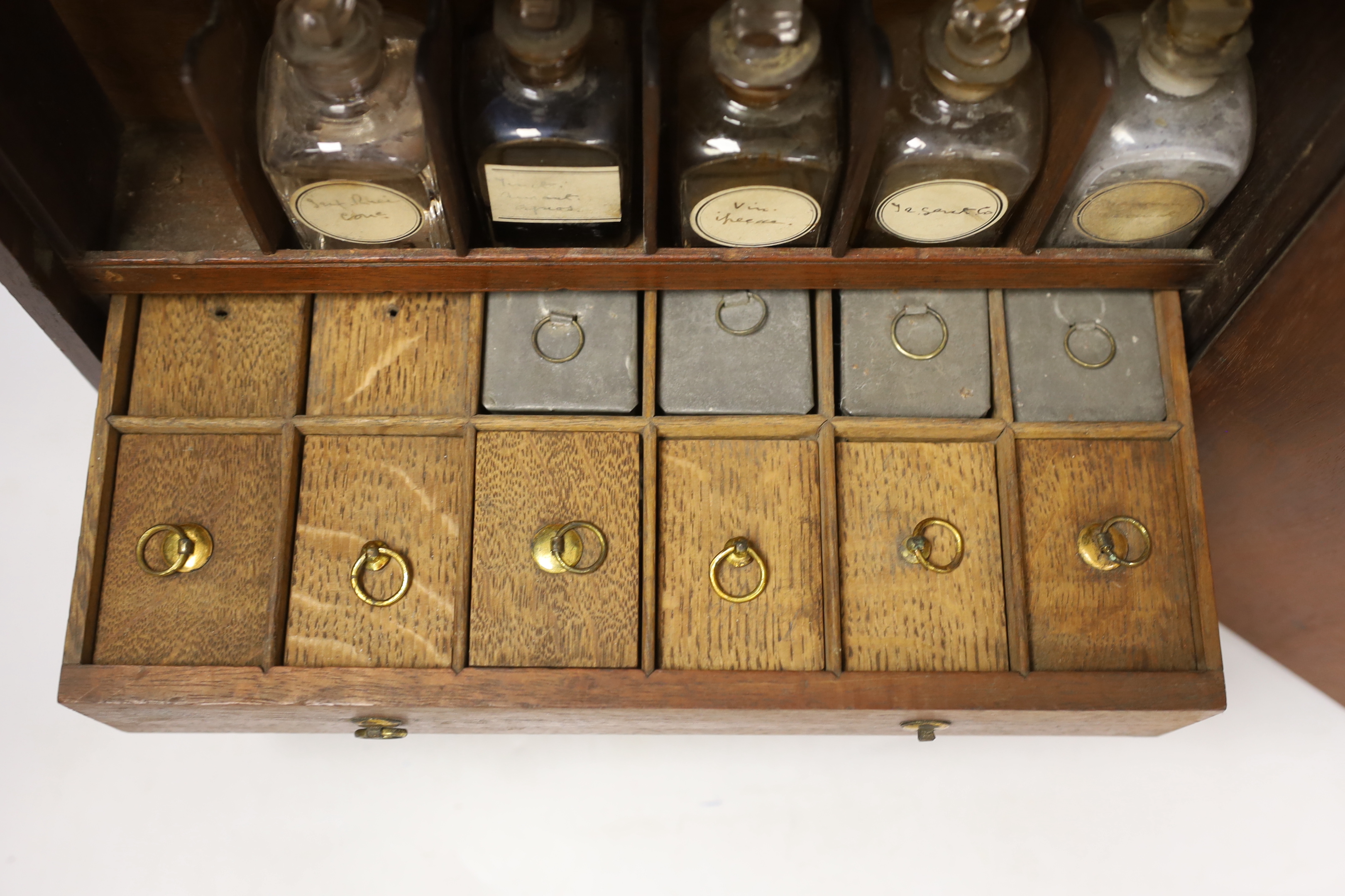 An early 19th century mahogany apothecary box, opening on both opposite sides and top lid, with fitted compartments and two drawers containing square section labelled glass bottles, oak and zinc lidded drawer sections, c